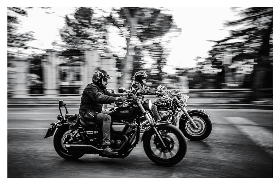 Two motorcyclists in a black-and-white panning photograph with the street blurred behind them.